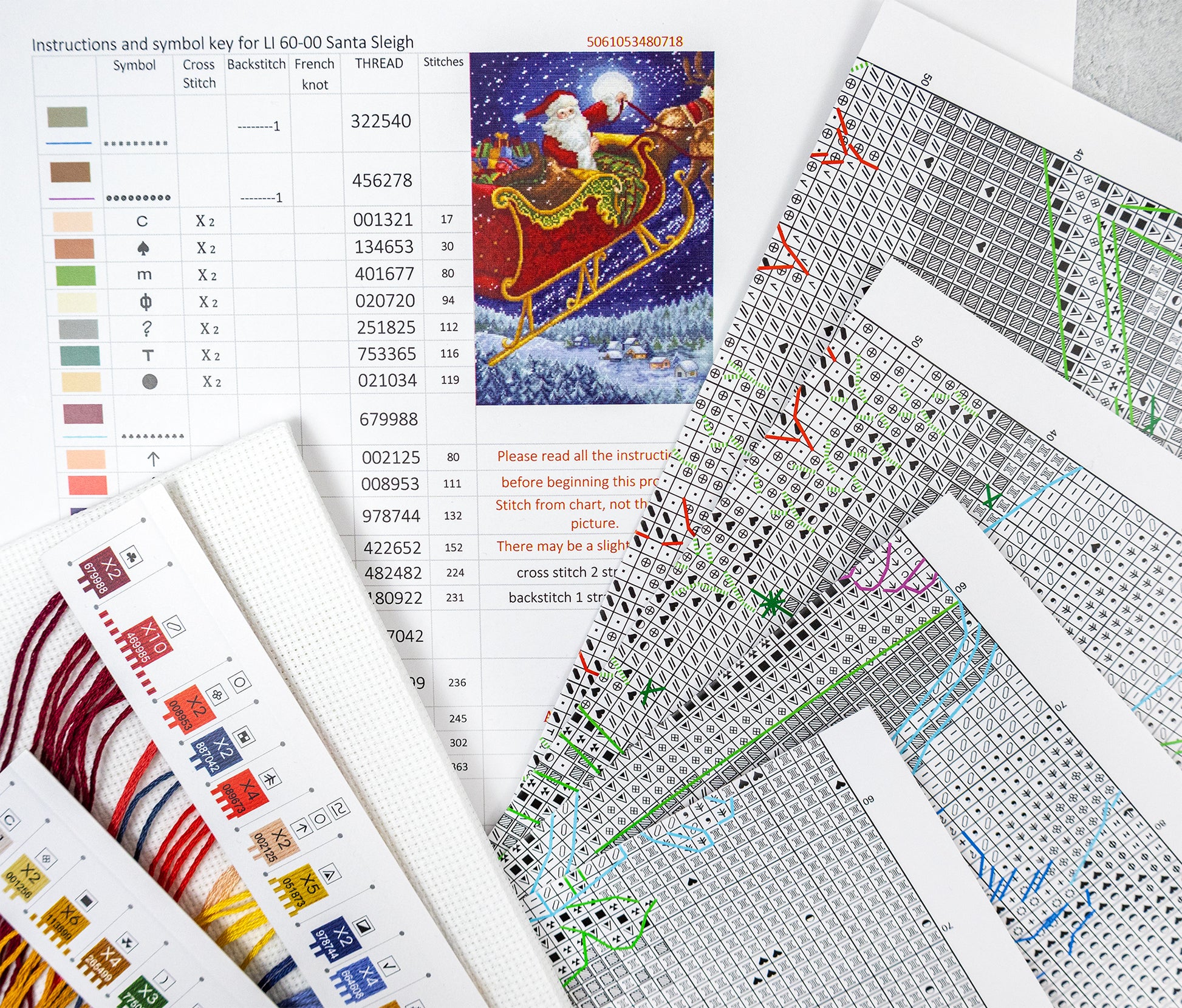 Cross-stitch pattern sheets with a Santa Claus sleigh design on a textured surface.
