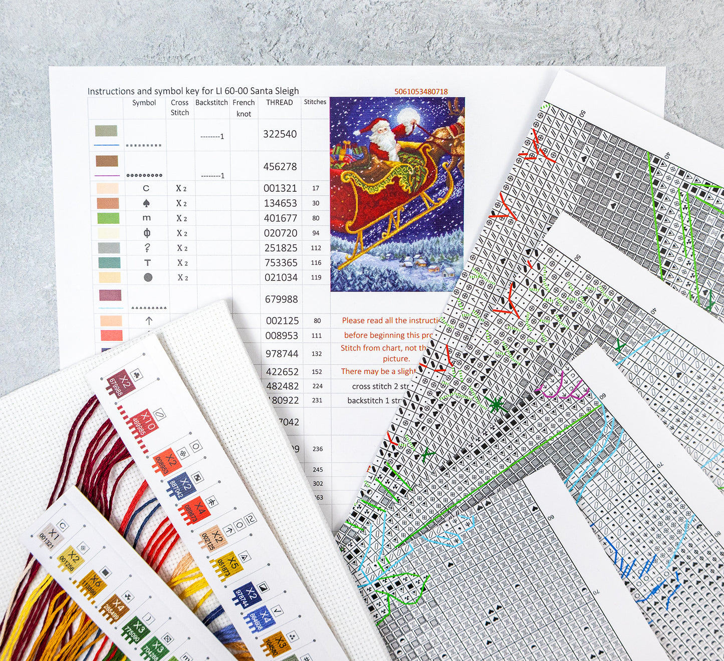 Cross-stitch pattern sheets with color chart and Santa Claus illustration on a gray surface