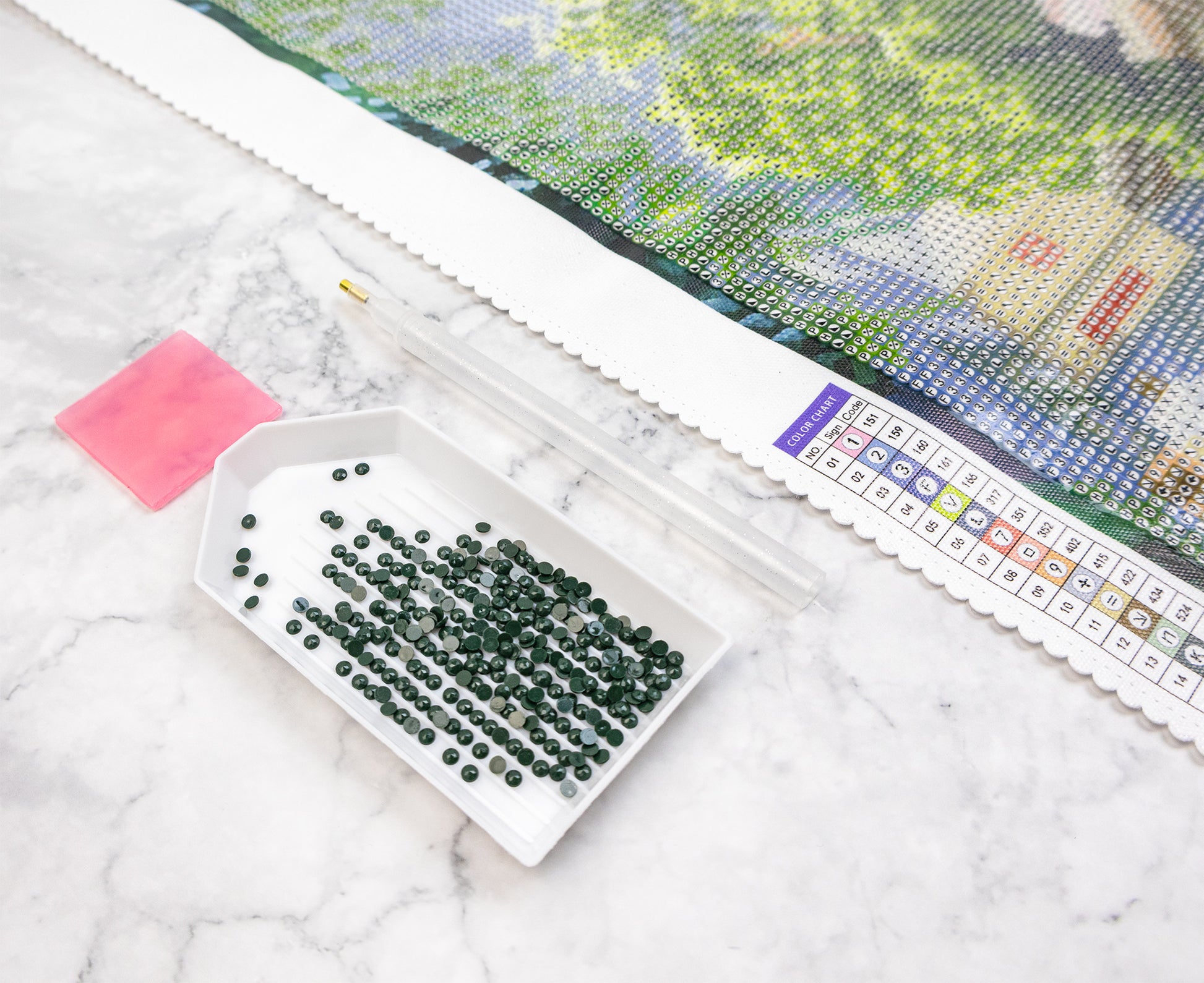 Box of green crystals next to a diamond art pattern on a marble surface