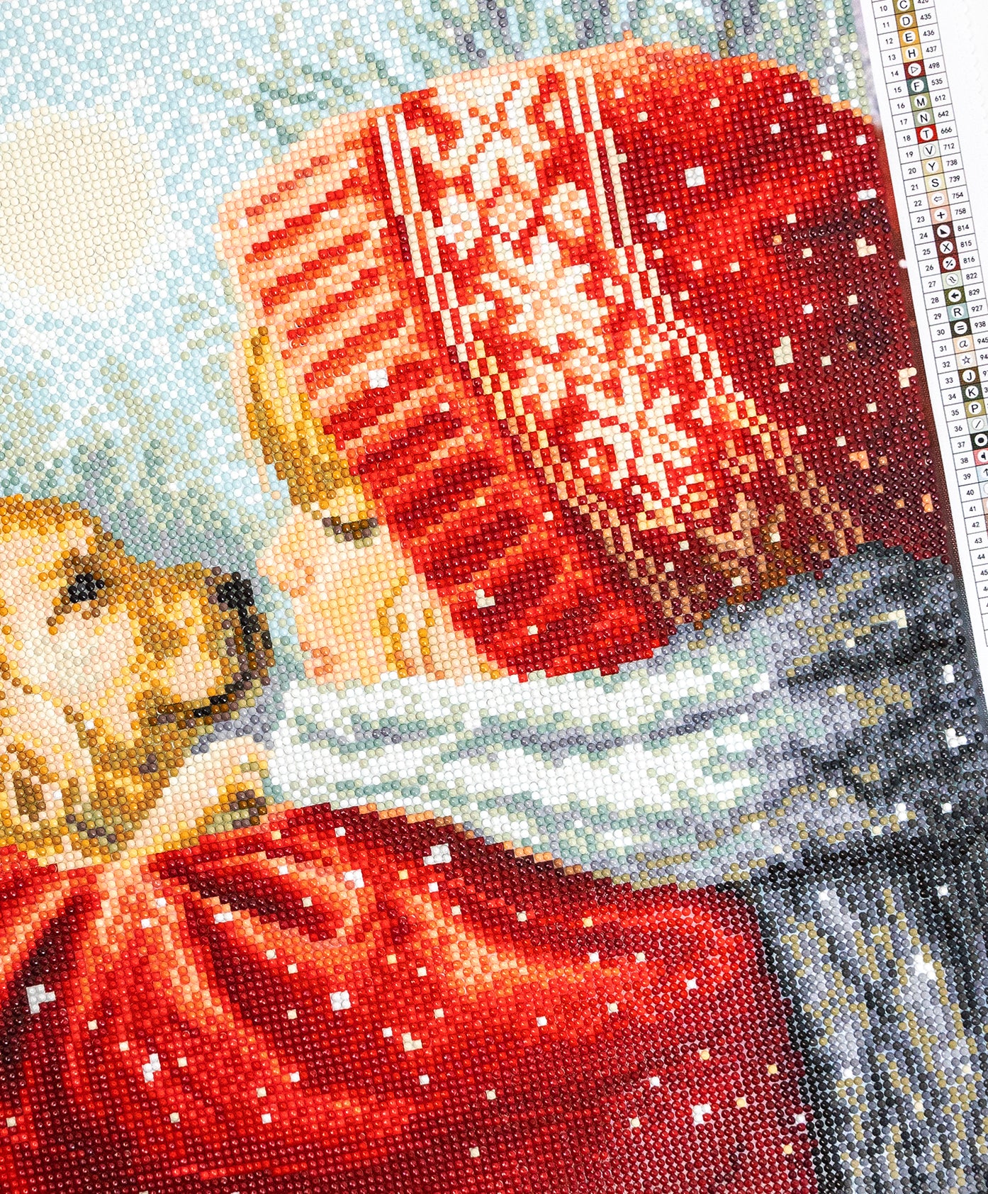 Close-up of a diamond painting piece with a red hat and scarf, featuring a pattern of snowflakes.
