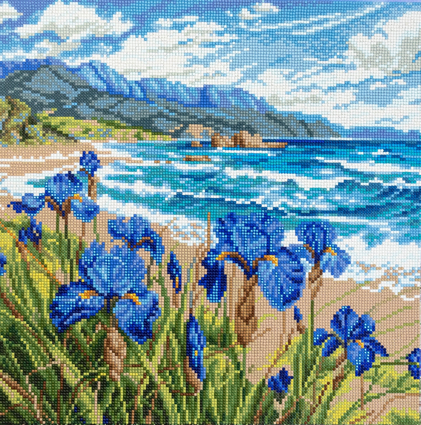 Diamond Art of blue flowers by a coastal landscape with mountains.