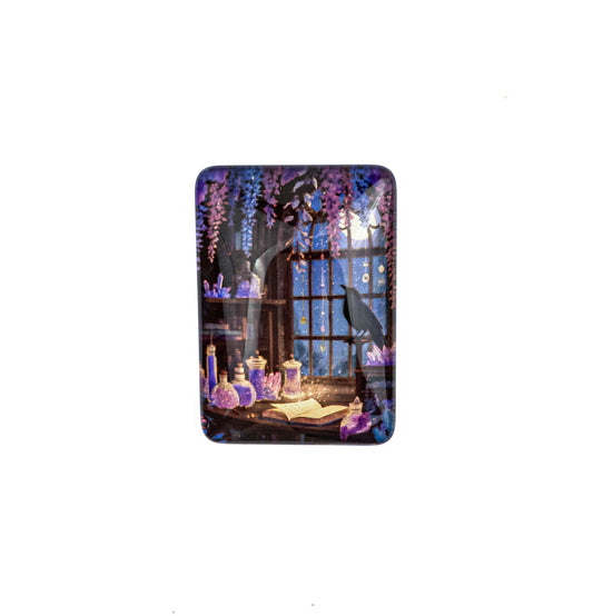 A rectangular magnet with rounded corners, decorated with a colorful illustration featuring a crawl in a library next to lantern pots, placed on a dark brown stone surface.